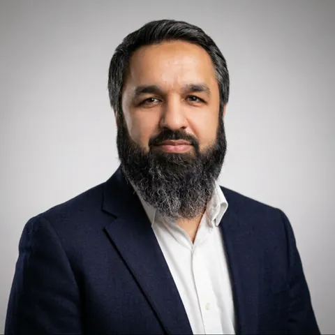 Umar Muhammad Sharif, studio portrait in a navy blazer and white shirt against a grey background